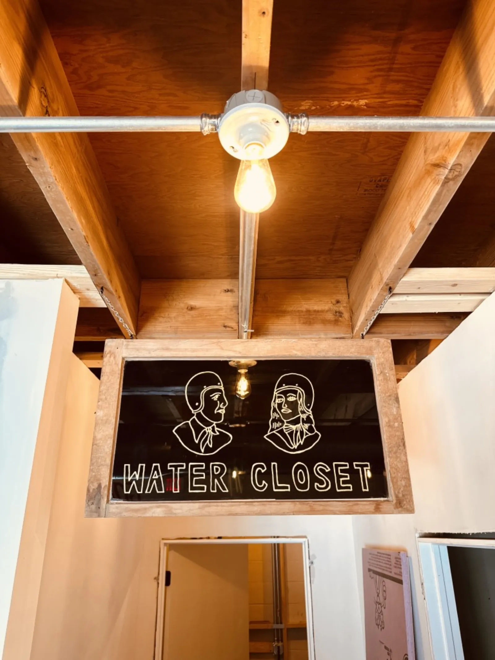 Hand-lettered "Water Closet" glass sign with Edison bulb at Moon Wolf — brand-as-craft signal.
